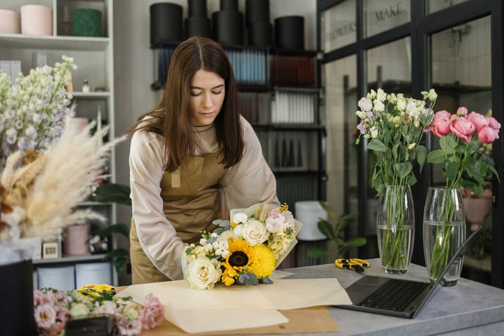 Portrait Of Young Brunette Female Florist Holding Bouquet Of Flowers And Looking At Them.